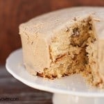 A butter pecan cake on a cake stand with a triangle piece cut out of it