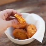 A woman holding a cornbread cheddar bite above a bowl of bites.