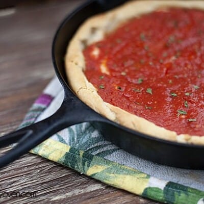 A cast-iron skillet with pizza dough and tomato sauce on it.
