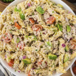 Cold tuna pasta salad in white bowl surrounded by fresh vegetables.