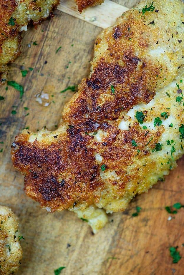 Parmesan chicken breast on a wood cutting board.