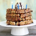 A stack of waffles with birthday candles on top on a cake stand