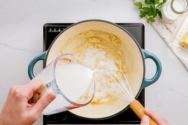 milk pouring into pot to make a cheese sauce.