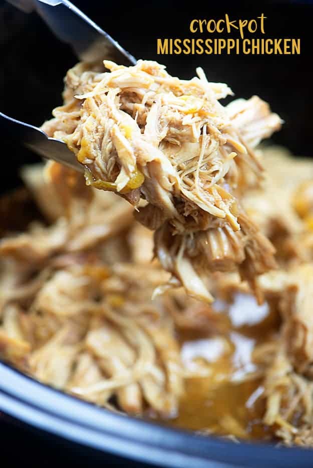 Shredded chicken being held up by metal tongs.