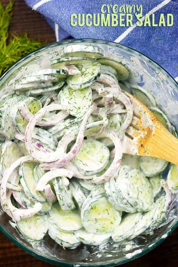 A clear glass bowl full of cucumbers and onions.