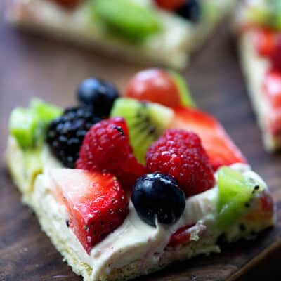 A square piece of fruit pizza on a wooden table.