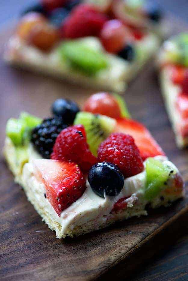 A square piece of fruit pizza on a wooden table.