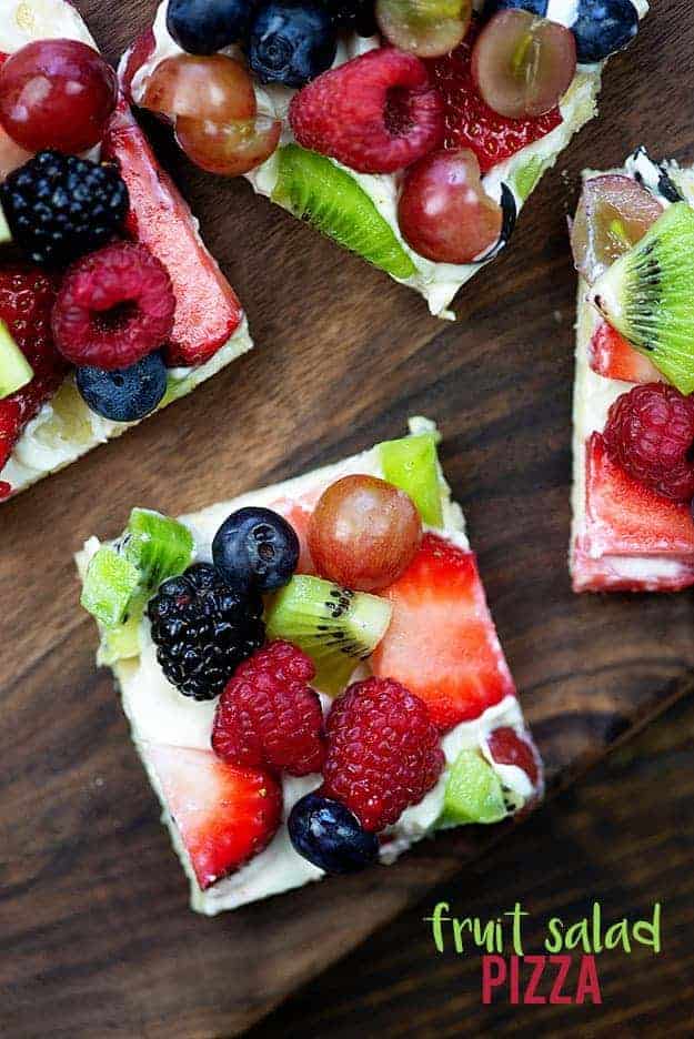 Several square fruit pizzas on a wooden table.