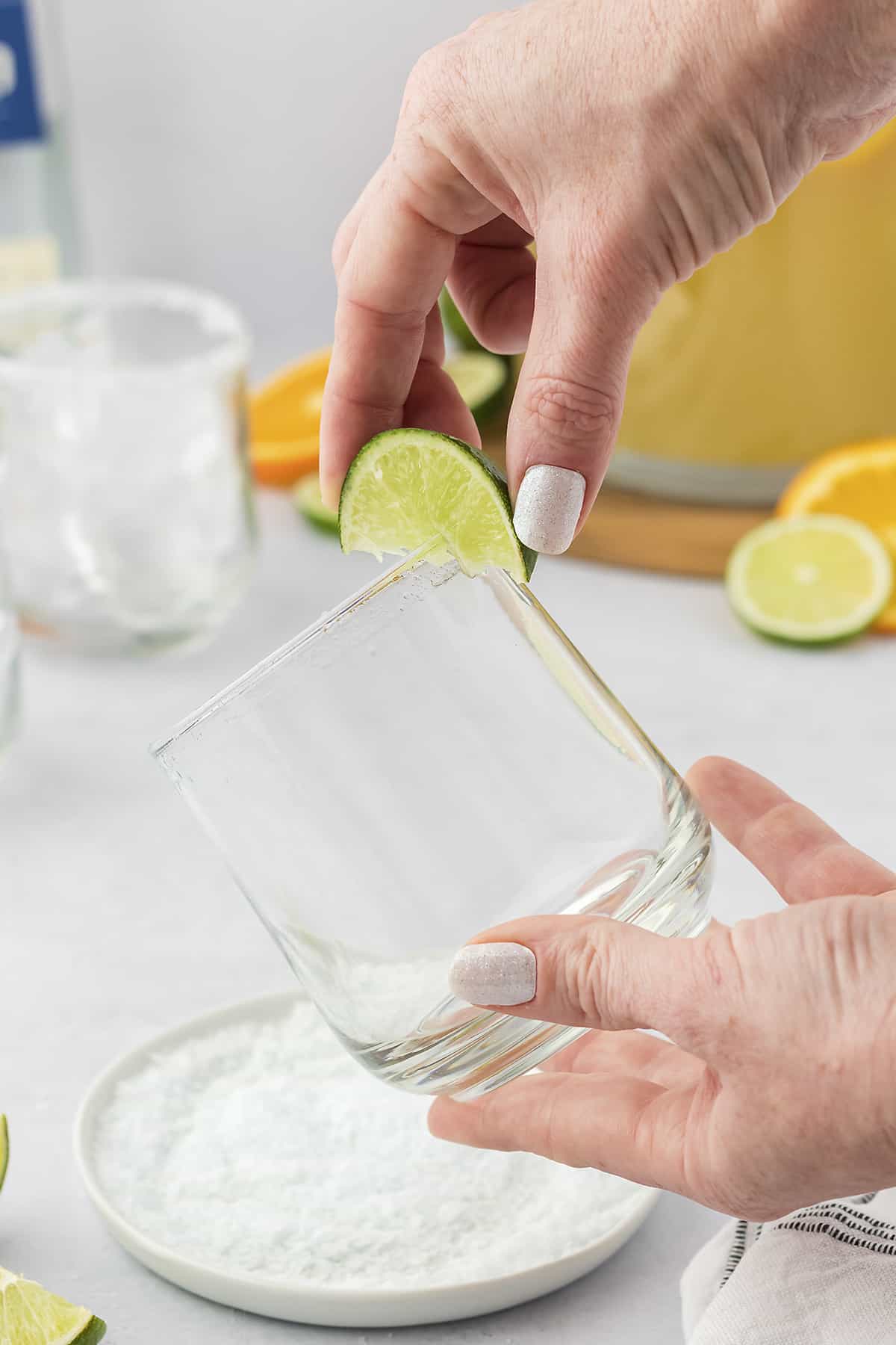 Hand rubbing a lime wedge around the edge of a glass.