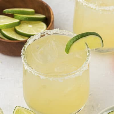 Homemade margarita on the rocks next to bowl of limes.