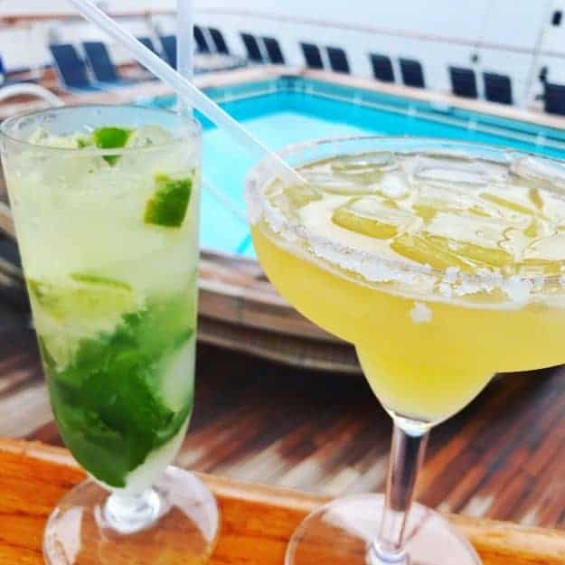 A mojito and a margarita on a poolside railing.