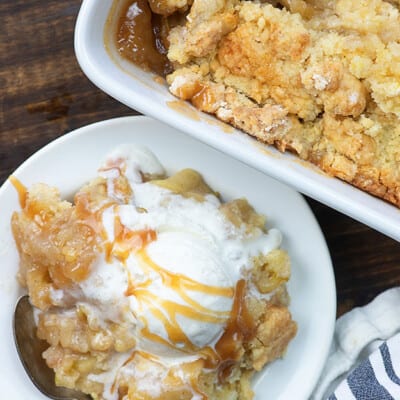 Apple cobbler on a white plate topped with vanilla ice cream and drizzled with caramel.