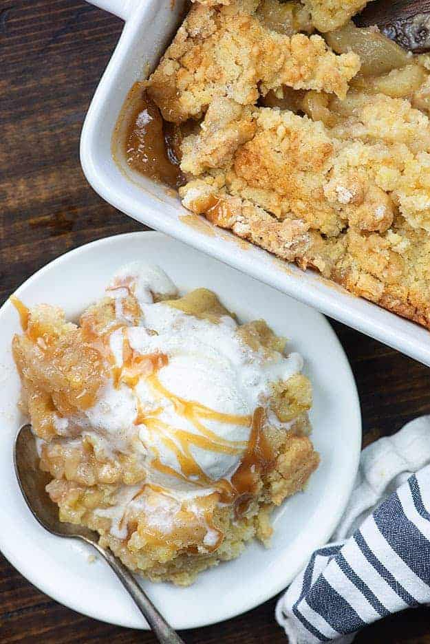 Apple cobbler on a white plate topped with vanilla ice cream and drizzled with caramel.