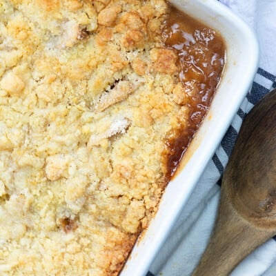 Apple cobbler in a white baking dish next to a wooden spoon.