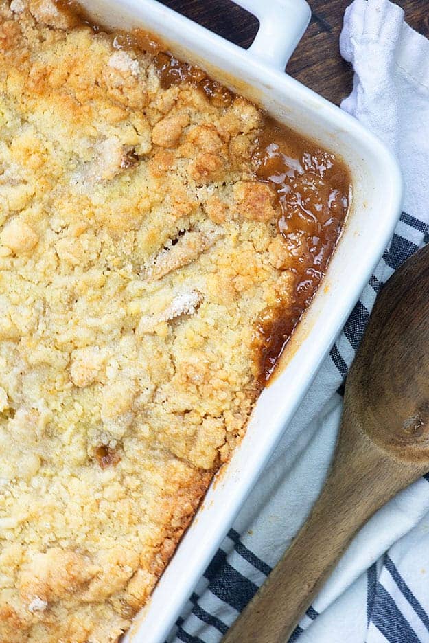 Apple cobbler in a white baking dish next to a wooden spoon.