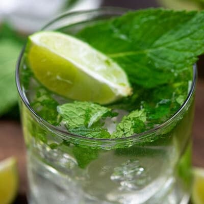 A glass of a mojito topped with mint leaves and lime.