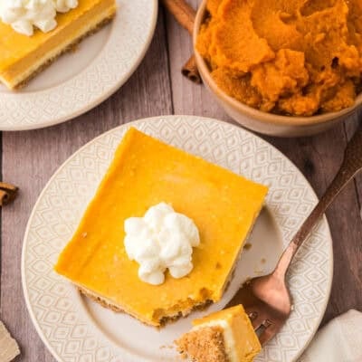Pumpkin cheesecake bar on white plate with a fork.