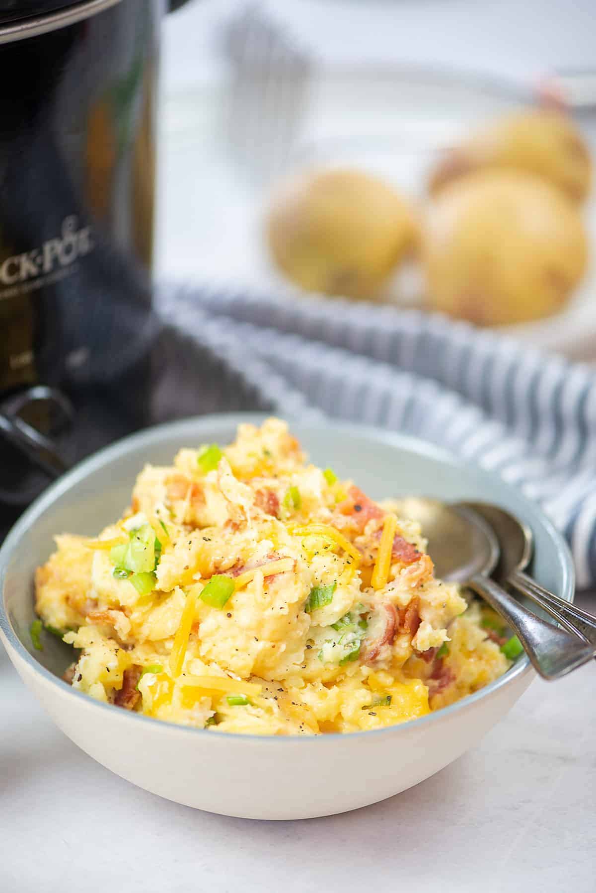 loaded mashed potatoes in bowl next to crockpot.