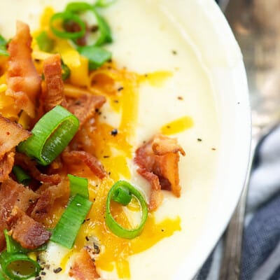 Potato soup in a white bowl topped with cheese, bacon, and chives.