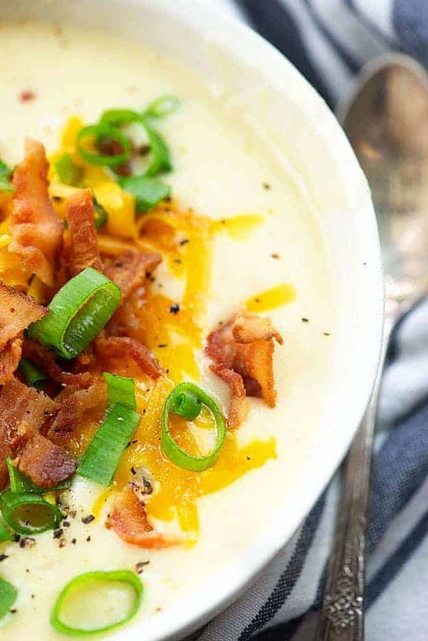 Potato soup in a white bowl topped with cheese, bacon, and chives.