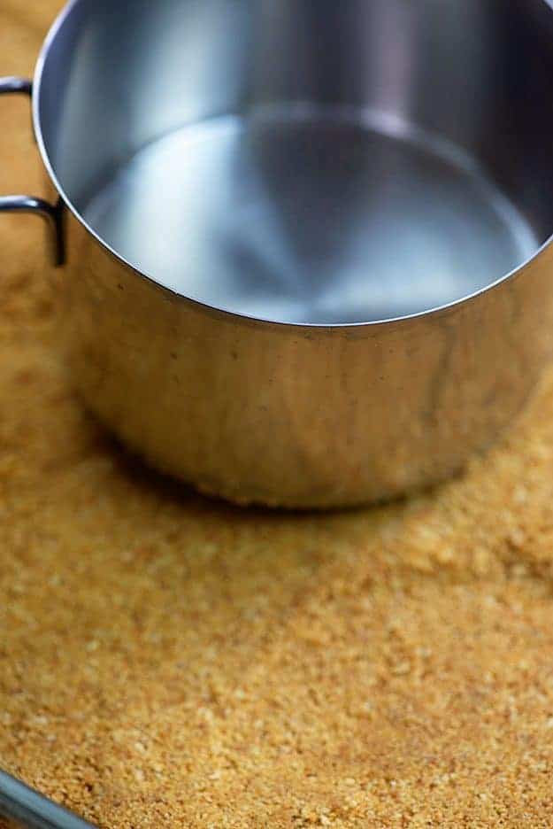 pressing graham cracker crust into pan with measuring cup