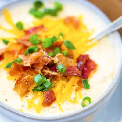 Crockpot potato soup topped with cheddar and green onion in bowl.