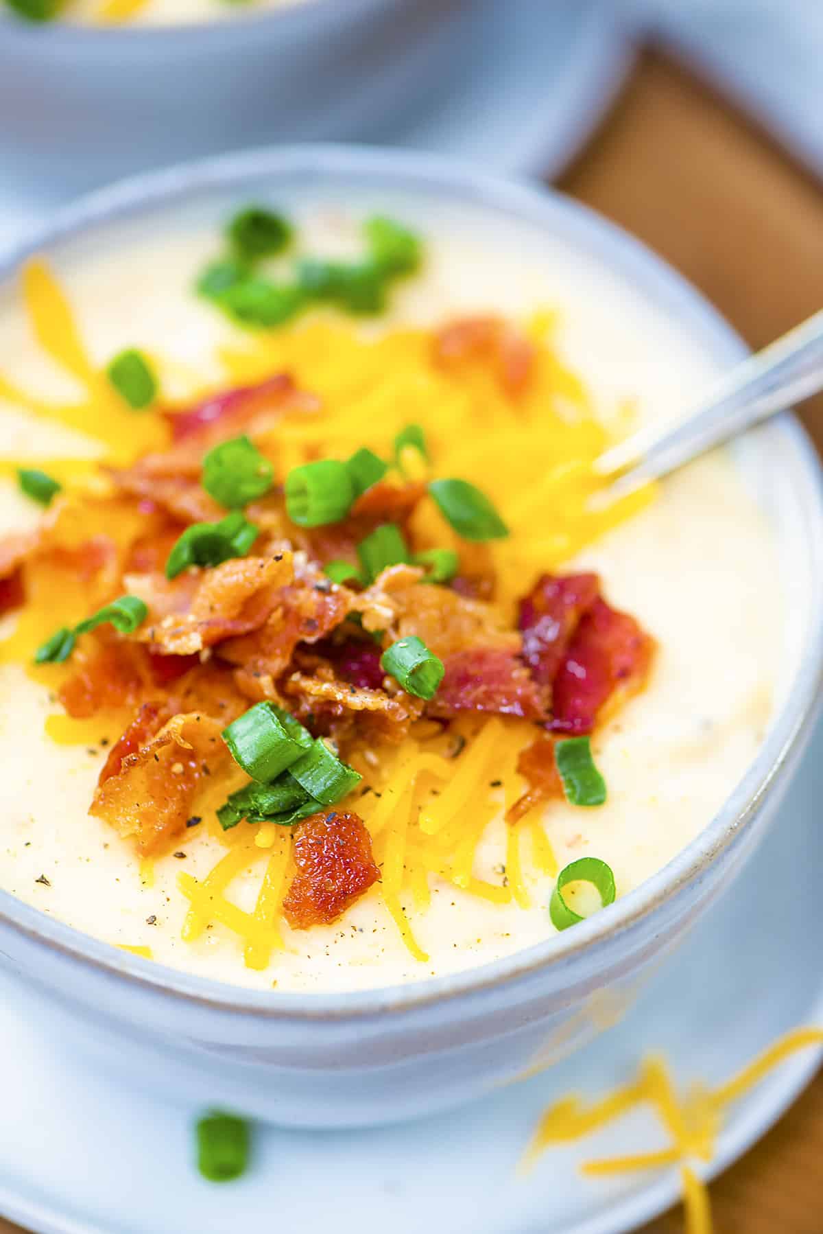 Crockpot potato soup topped with cheddar and green onion in bowl.