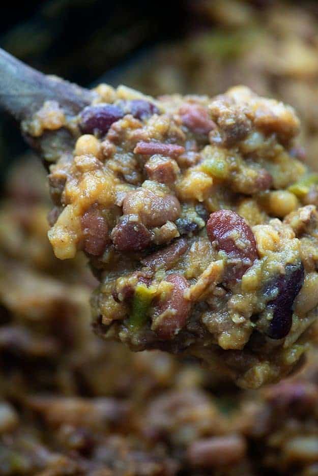 A close up of a wooden spoon of beef and beans.