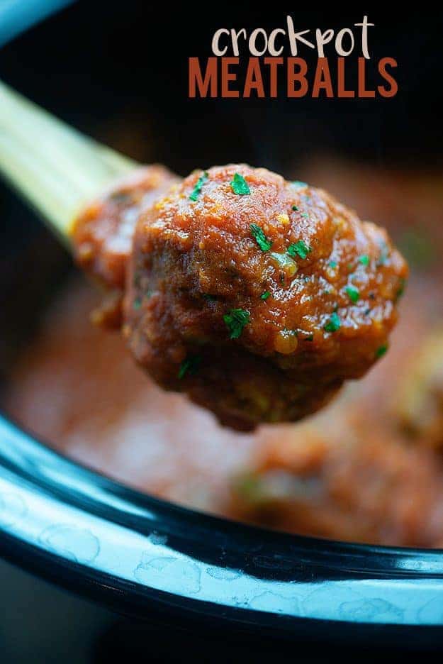 A close up of a meatball on a wooden spoon.