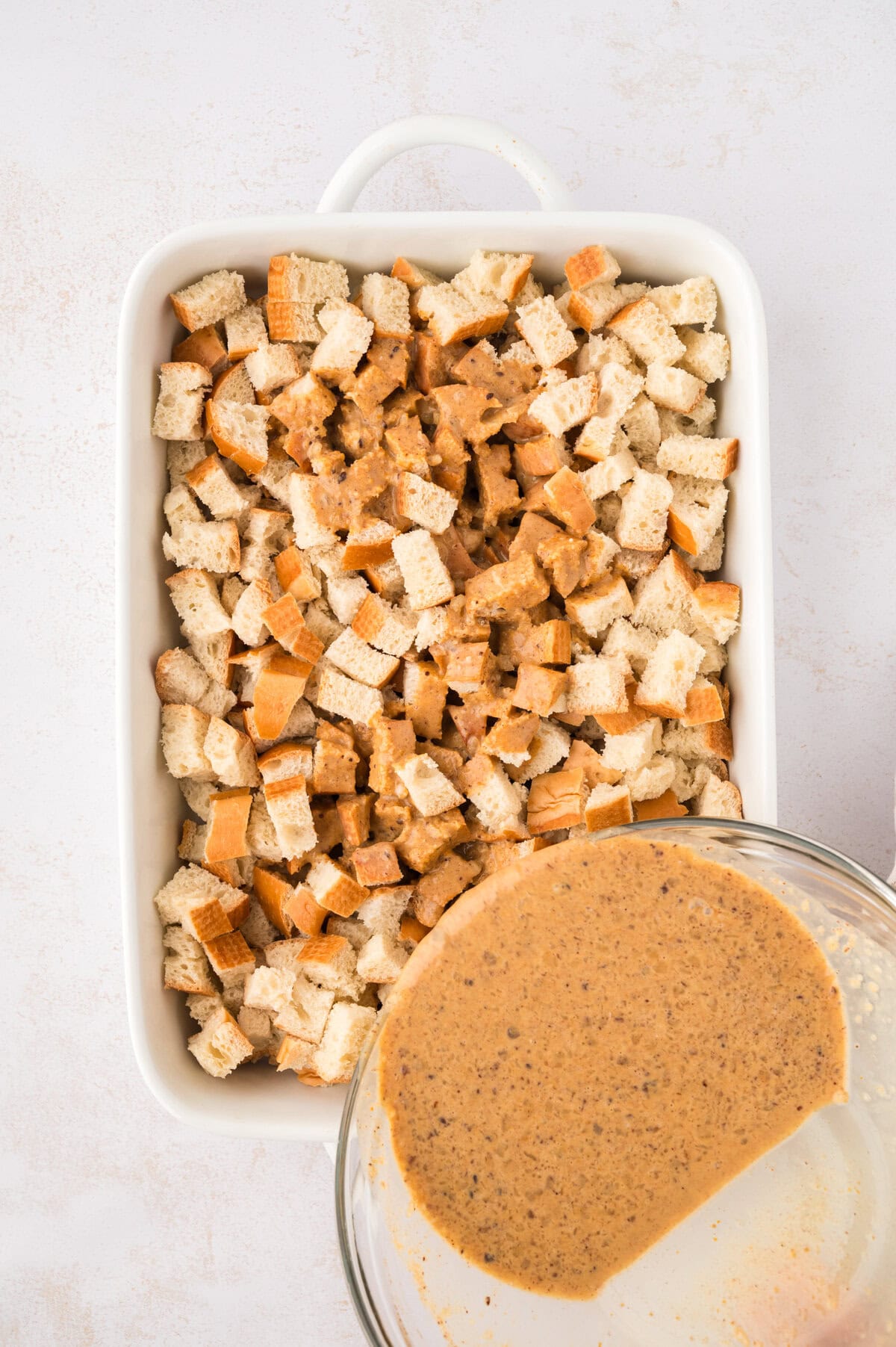 Pumpkin custard being poured over cubed bread.