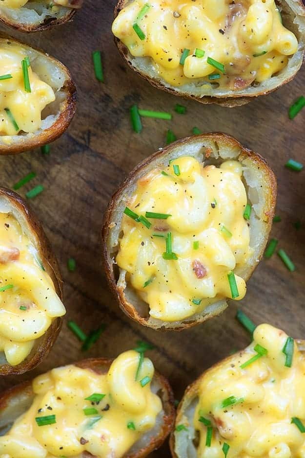 Several potato halves topped with mac n cheese on a cutting board.