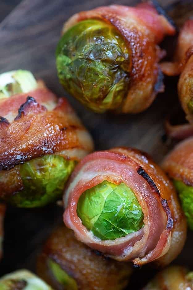 Several bacon wrapped brussel sprouts on a cutting board.