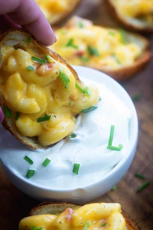 A close up of a macaroni and cheese potato being dipped into sour cream.