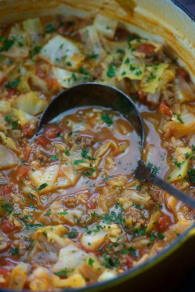 A crockpot of cabbage soup with a ladle dipping into it.