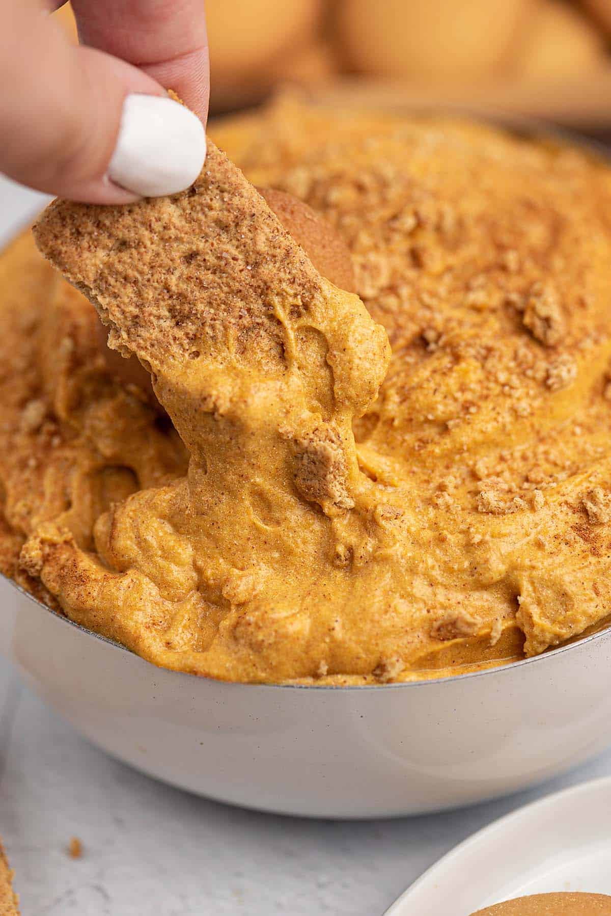 woman dipping a graham cracker in pumpkin dip.