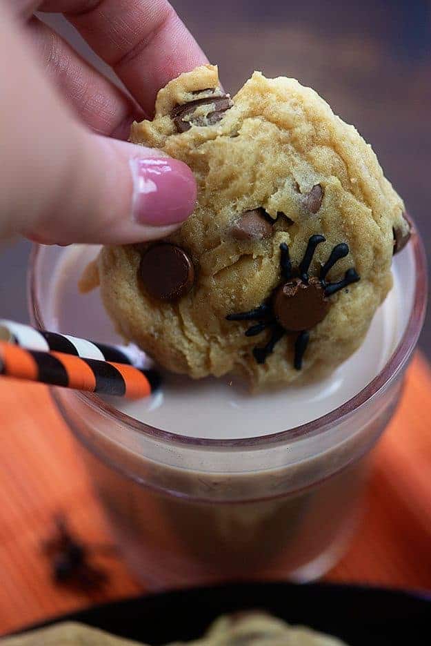 A close up of a cup of a woman dipping a chocolate chip cookie into a glass of milk.