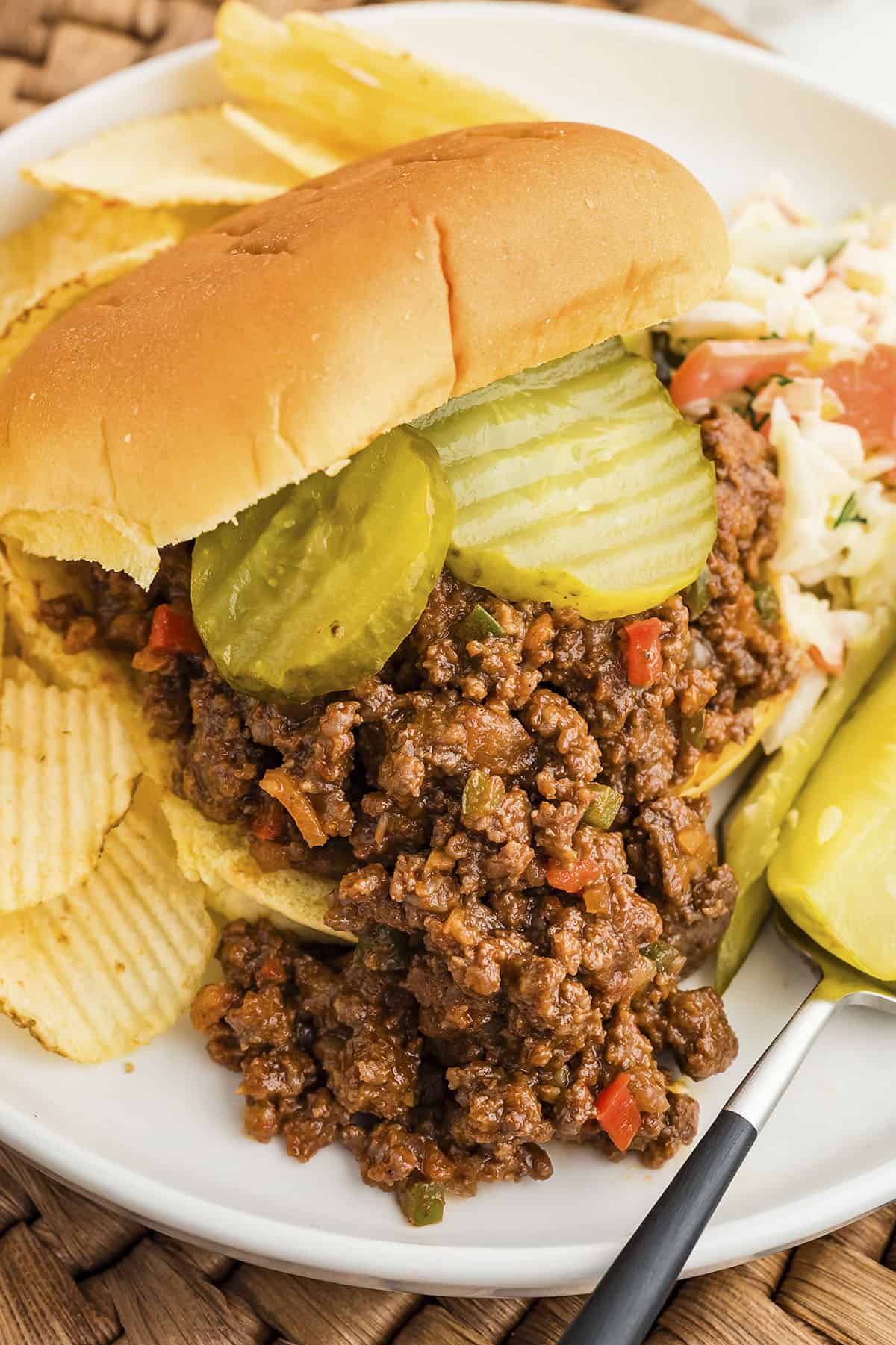 Homemade sloppy joe sandwich on white plate with chips and pickles.