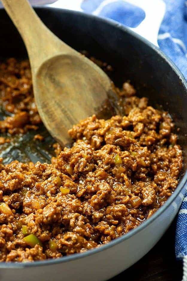 Sloppy joe in a skillet being stirred by a wooden spoon.