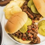 Sloppy joe sandwiches on white plate with chips.