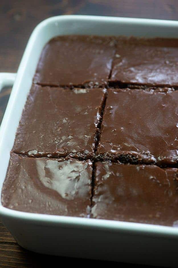 A close up of a chocolate cake cut into squares in a cake pan.