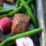 A close up a chunk of pork, radishes, and green beans on a sheet pan.