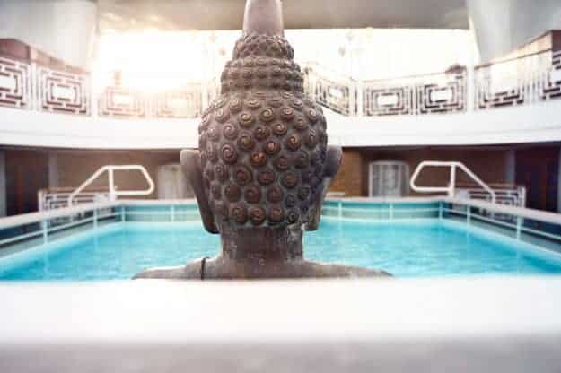 The back of a statues head in front of a pool of water.
