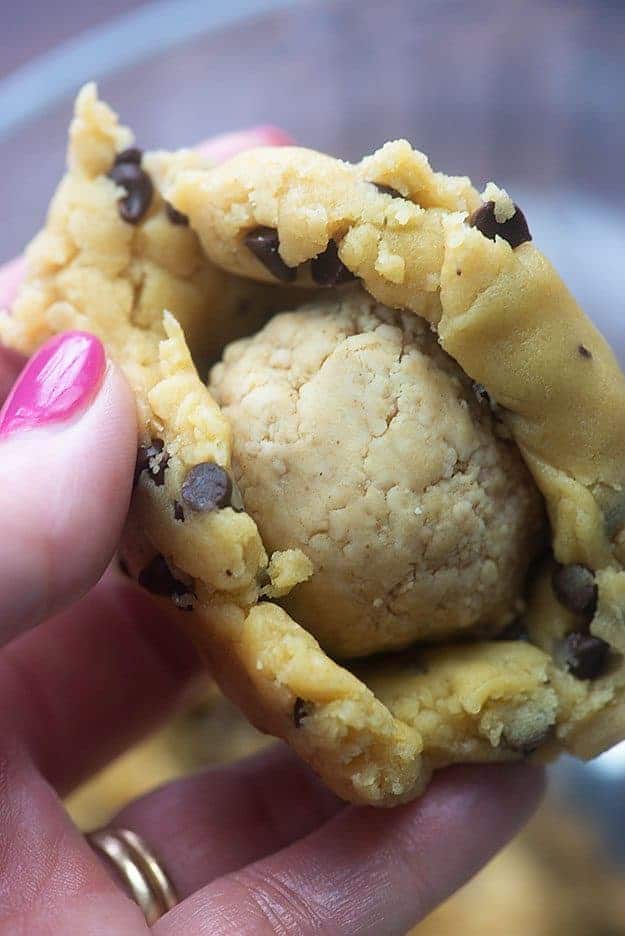 A woman holding peanut butter dough inside a wrap of cookie dough.