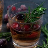 A glass of sangria on a table with rosemary.