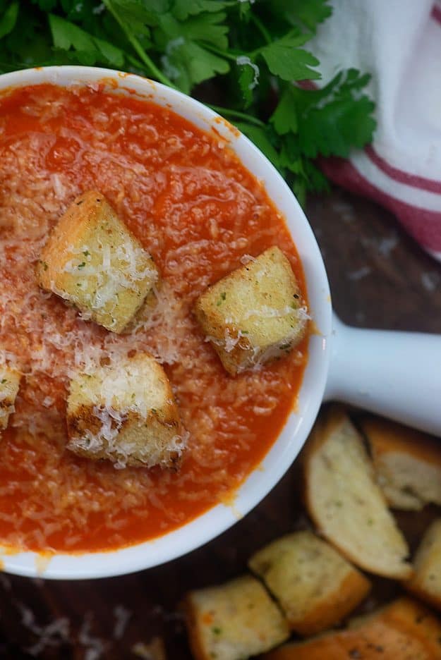 A white bowl of tomato soup topped with croutons 