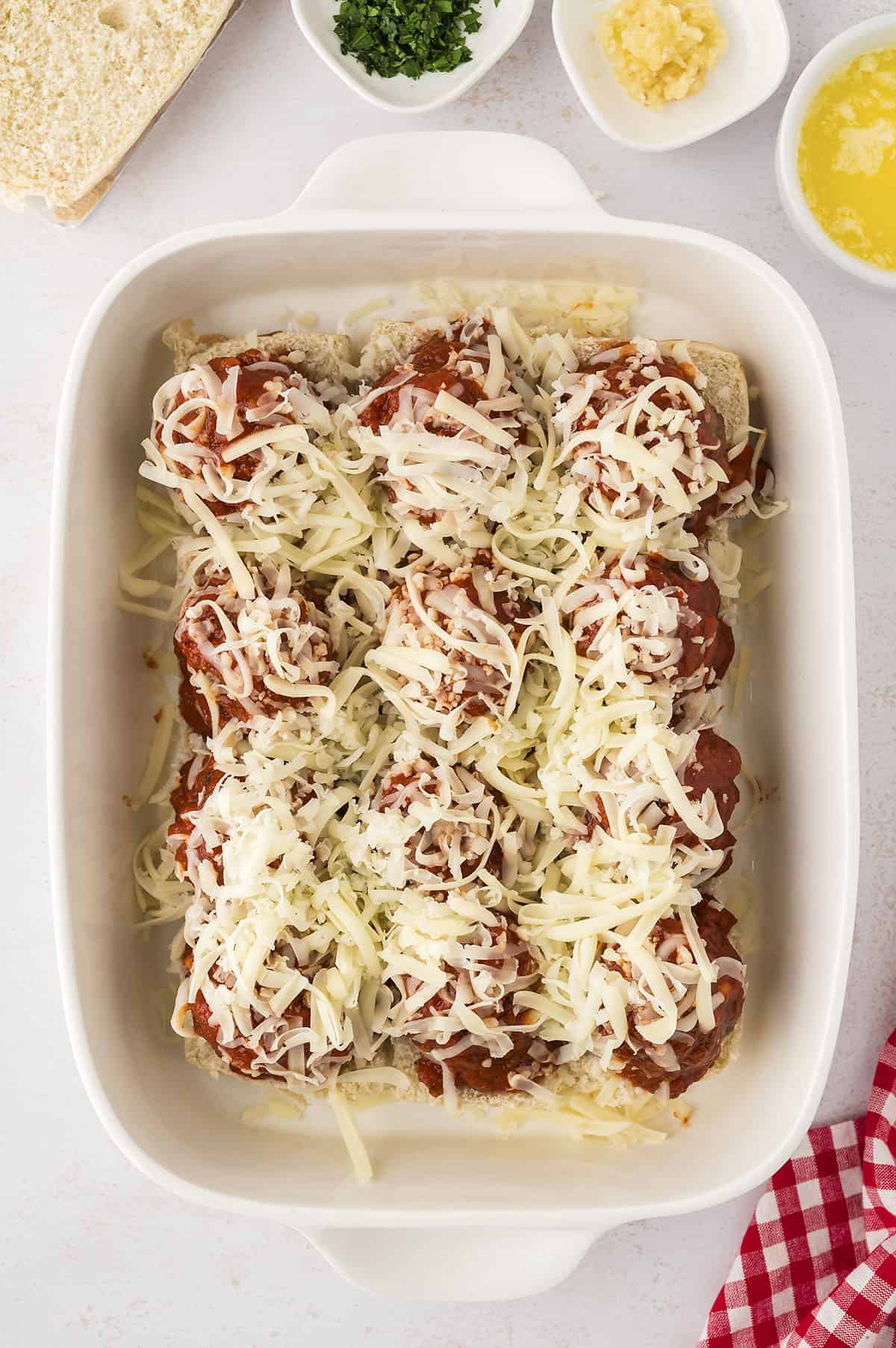 Meatballs covered in marinara and cheese on sliders.
