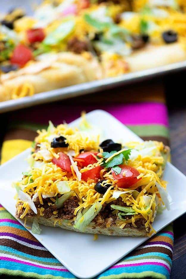 A square piece of taco pizza on a square plate.