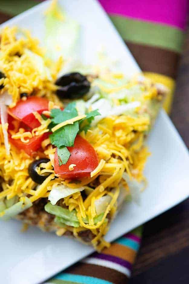 A slice of taco pizza on a square plate.