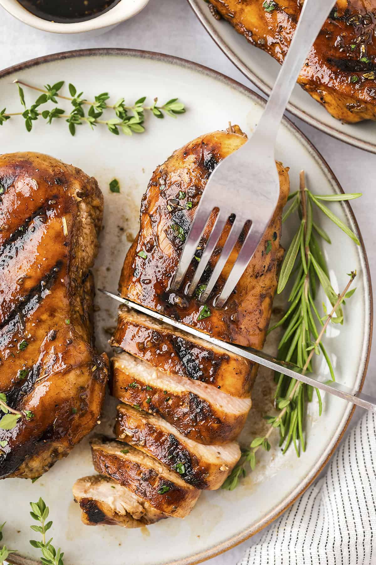 Balsamic chicken on plate being cut with a knife and fork.
