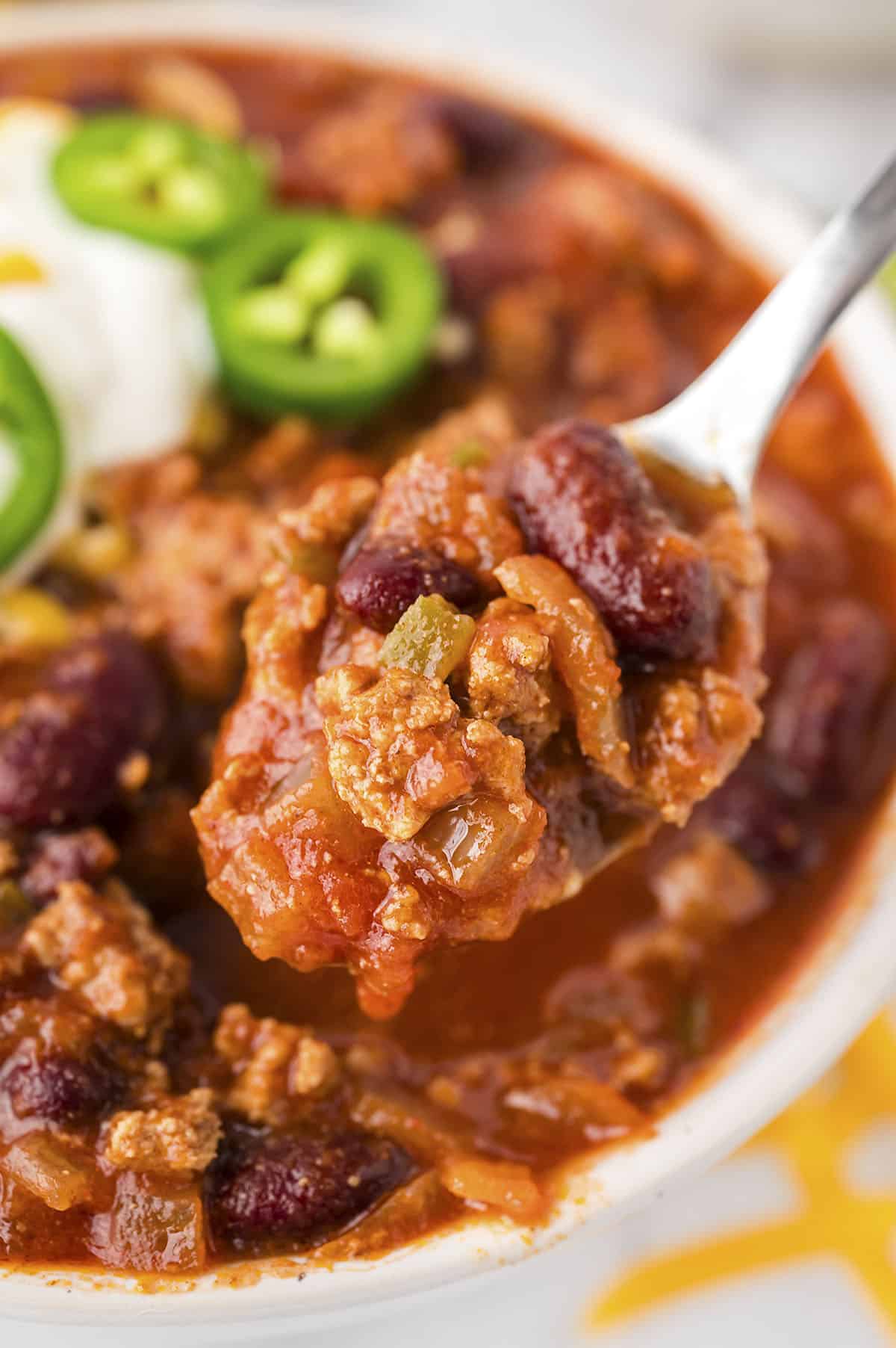A spoonful of chili held up to the camera above a bowl of chili.